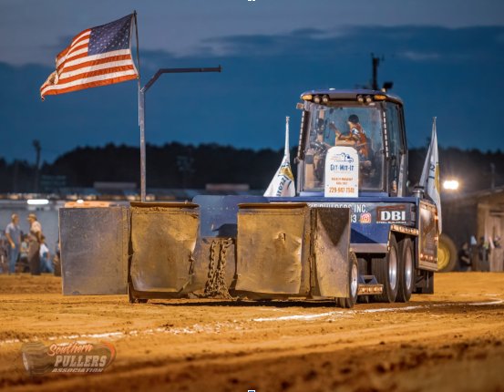 A tractor pulling the SPA sled down the track under the lights